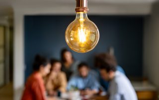 Light bulb in focus with group of people in collaboration blurred in the background