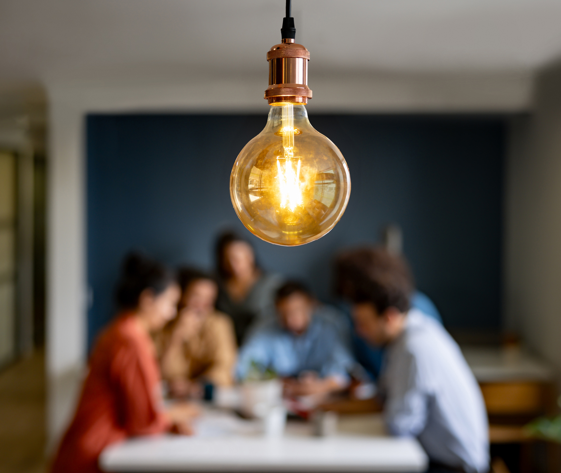 Light bulb in focus with group of people in collaboration blurred in the background